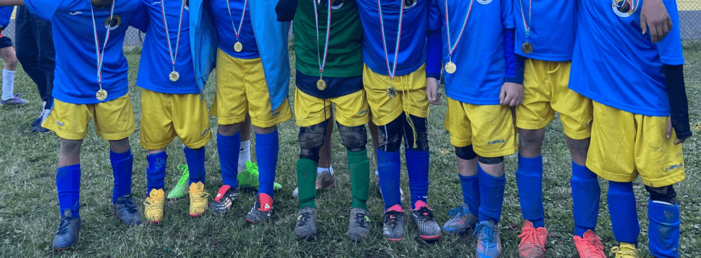Squadra di calcio giovanile in divisa blu e gialla con medaglie al collo, schierata sul campo da gioco.